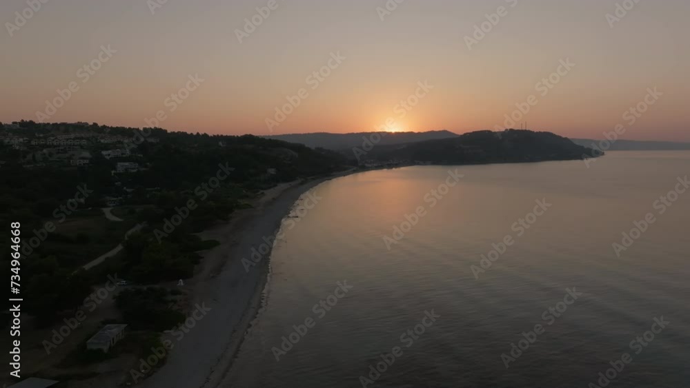 Drone shot of beach, sea, and sunrise with a silhouette of a hill Drone shot of beach, sea, and sunrise with a silhouette of a hill