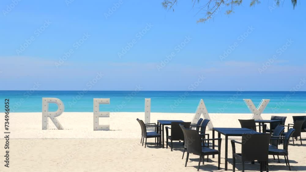 Tropical beachfront cafe setting with large 'RELAX' sign on pristine sandy shore, inviting calmness and peacefulness amidst natural coastal environment. Leisure and tourism. Tropical beachfront cafe setting with large 'RELAX' sign on pristine sandy shore, inviting calmness and peacefulness amidst natural coastal environment. Leisure and tourism.