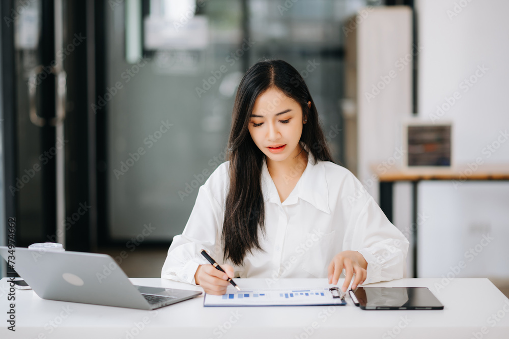 Asian businesswoman working with working notepad, tablet and laptop documents talking on the tablet and laptop Asian businesswoman working with working notepad, tablet and laptop documents talking on the tablet and laptop