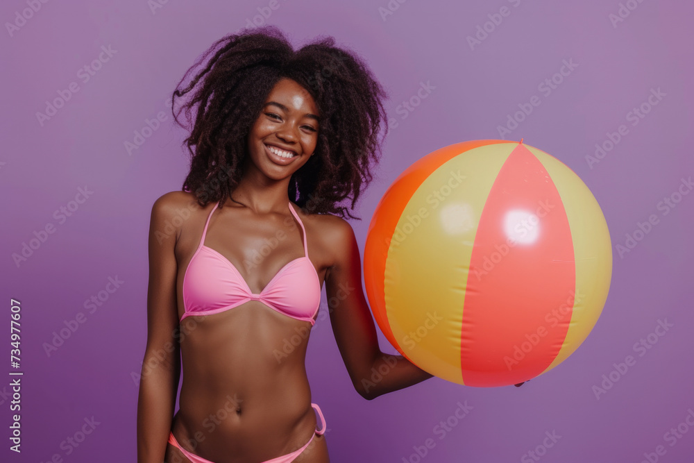 Funny young happy African American woman in swimsuit having fun holding inflatable ball and going on summer holiday trip standing on purple studio background. Vacation tour and travel concept. Funny young happy African American woman in swimsuit having fun holding inflatable ball and going on summer holiday trip standing on purple studio background. Vacation tour and travel concept.
