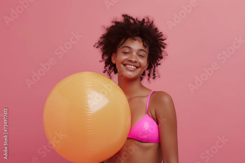 Funny young happy African American woman in swimsuit having fun holding inflatable ball and going on summer holiday trip standing on pink studio background. Vacation tour and travel concept. © AI_images