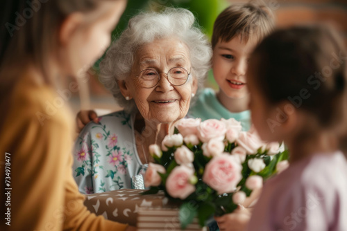 Happy senior woman receives presents from her grandchildren. Children make their grandmother a birthday surprise. Little kids give their grandma a gift card and a bouquet of flowers © AI_images