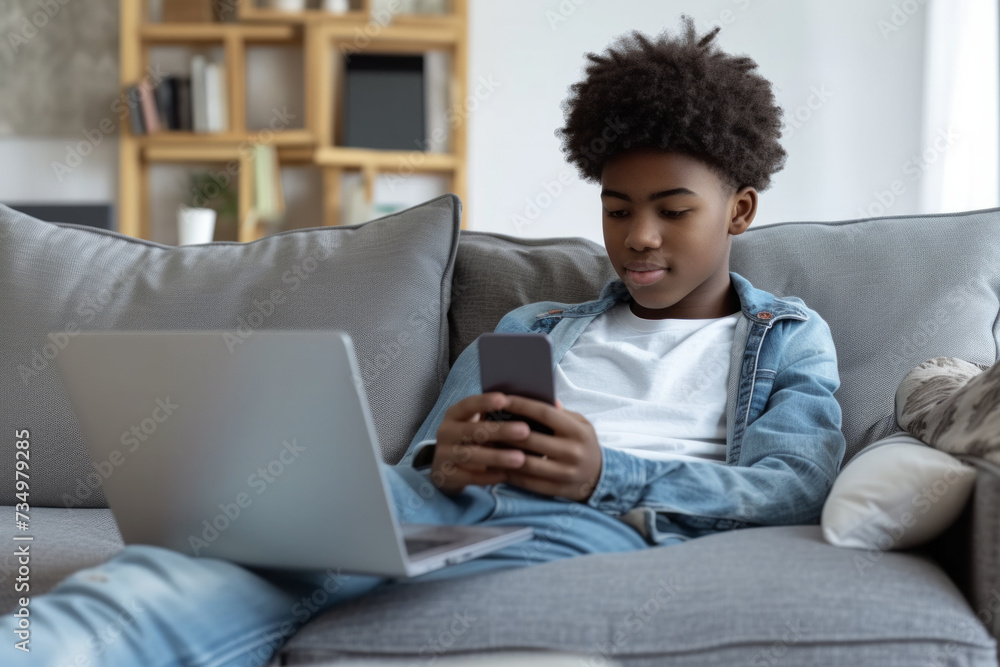 Young ethnic African American boy teenager uses laptop to chat with friends and use social networks on Internet sits on sofa with portable computer on lap. Digital addiction Young ethnic African American boy teenager uses laptop to chat with friends and use social networks on Internet sits on sofa with portable computer on lap. Digital addiction