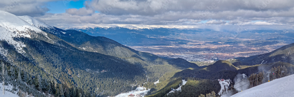 Panoramic view to the beautiful town of Bansko seen behind the evergreen forest and mountain hills at the horizon