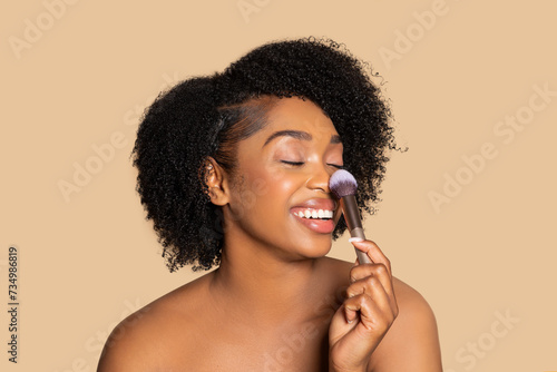Joyful black woman applying blush with makeup brush