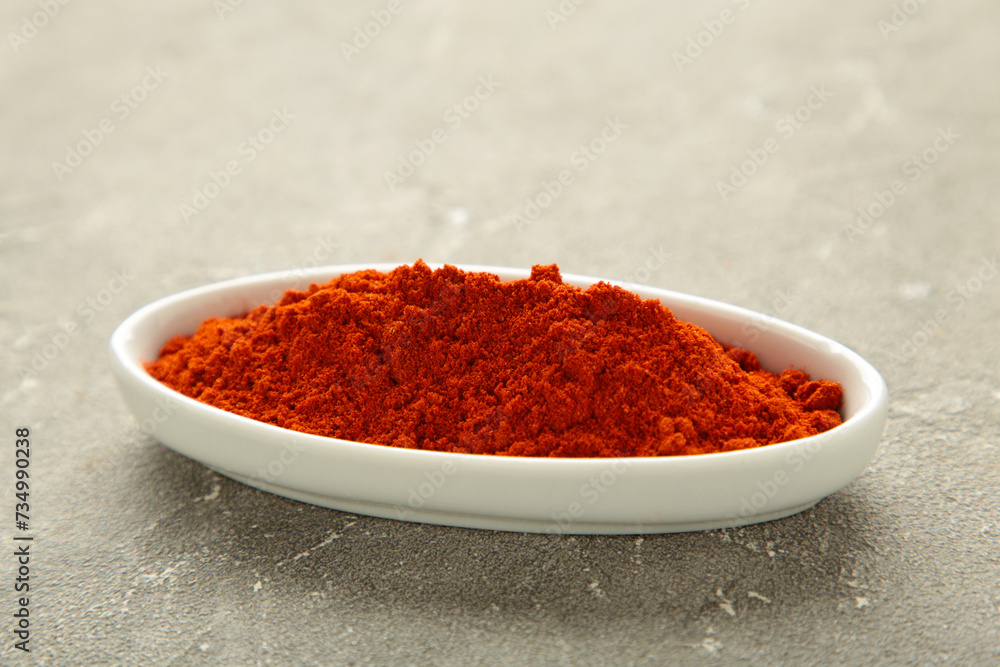 Red sweet paprika powder on plate on grey background Red sweet paprika powder on plate on grey background