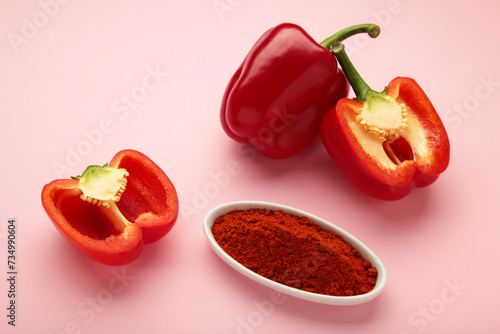 Paprika powder in plate with fresh red pepper on pink background.