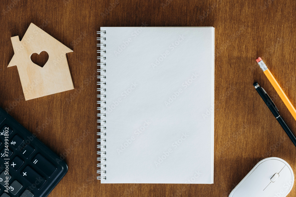 Blank notebook, calculator and model of a house on a wooden table. Planning to buy a home, calculating taxes, paying bills. Blank notebook, calculator and model of a house on a wooden table. Planning to buy a home, calculating taxes, paying bills.