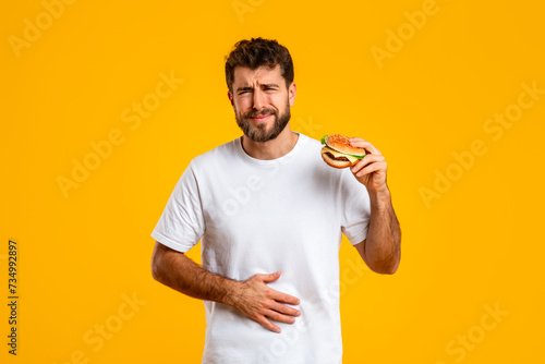 Foto man experiences stomach discomfort after consuming burger on yellow background