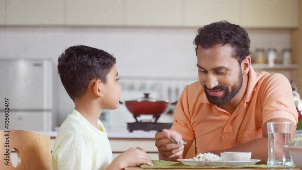 Happy father feeding His child by talking and encouraging at home - concept of fatherhood, affection and family bonding Happy father feeding His child by talking and encouraging at home - concept of fatherhood, affection and family bonding