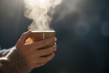 person holding a mug, steam drifting up against a dark background