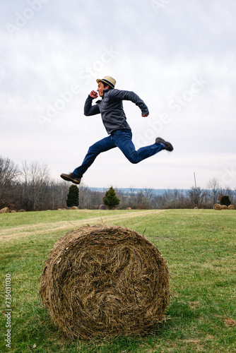 A man jumping high in the air over a round hay bail in a field