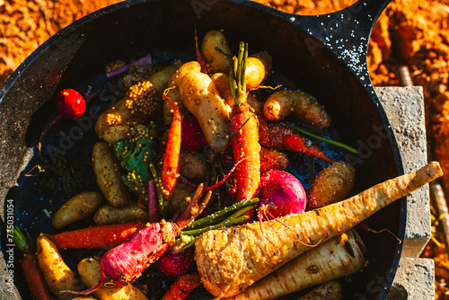 Root vegetables cooking in a cast iron skillet over fire photo