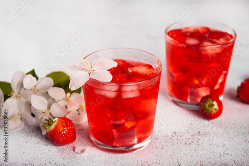 Strawberry cold refreshment lemonade with ice cube. White apple blossoms on the background. Spring concept.