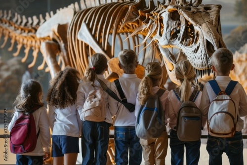 A group of school children view dinosaur skeletons in a museum during a field trip.
