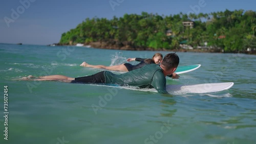 Surfers in swimwear paddling on surfboards. Man, woman in swimsuit swim on shore after session. Couple in love goes from water on boards. Family travel recreational activity. Relationship goals.