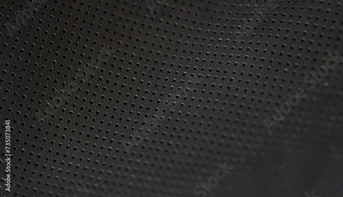 Black leather fabric pattern of small holes, close-up. Perforated matte texture. A macro shot of dark background