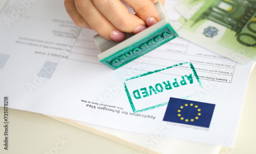 A hand puts a stamp approved on a document for a visa to Europe, close-up. Preparation of documents for a trip abroad