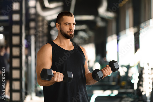 Portrait Of Motivated Male Athlete Exercising With Dumbbells At Fitness Club © Prostock-studio