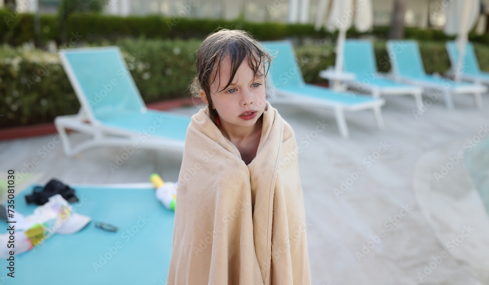 A small wet frozen child in a towel by the pool, close-up. Sun loungers for relaxing in the hotel, holidays with children