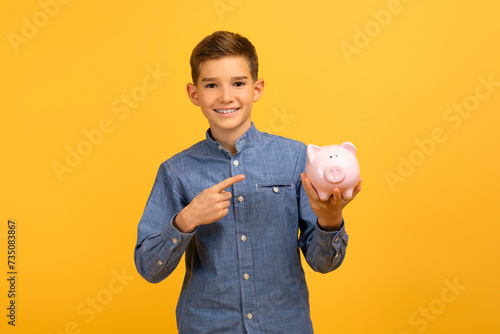 Happy excited teen boy pointing at piggy bank and looking at camera photo