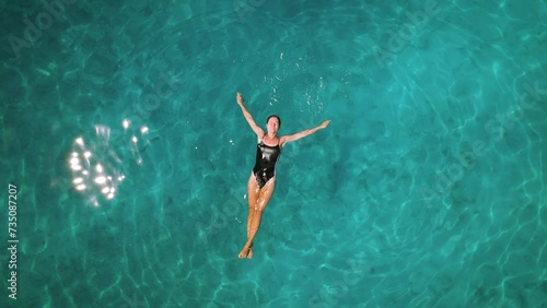 Serene swim in turquoise waters. A person floating peacefully in clear sea, aerial top down view of woman floating in ocean. photo
