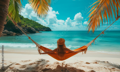 Fototapeta Naklejka Na Ścianę i Meble -  Happy beautiful girl in a straw hat and shorts, striped t-shirt, lying on a beach hammock between two palm trees, on the seashore of a tropical island.