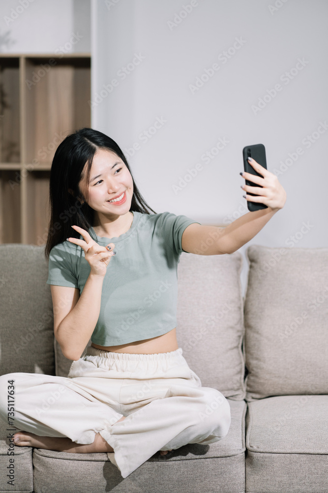 Happy woman having fun doing video call using mobile phone sitting on sofa, home office workplace lifestyle people.