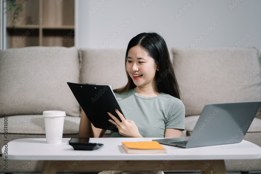 Woman sitting on sofa using mobile phone to calculate household expenses, hand holding account book for income-expense. Woman sitting on sofa using mobile phone to calculate household expenses, hand holding account book for income-expense.