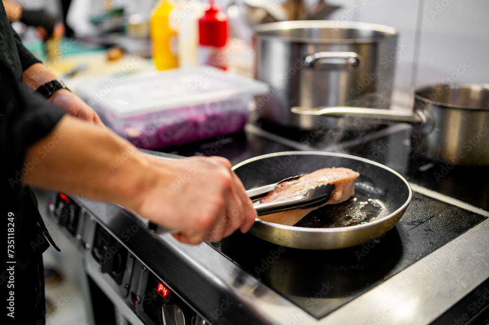 Professional chef cooking pork meat in frying pan on stove in restaurant kitchen