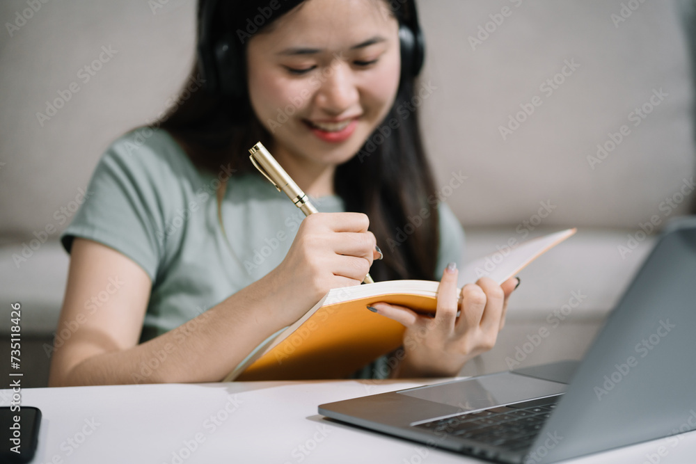 Smiling woman in headphones taking notes, motivated interested student studying online, using tablet, watching webinar training or listening to lecture, remote education concept.