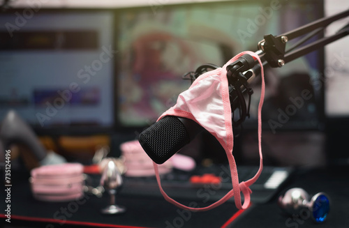 Women pink panties on a studio microphone with a metal anal plugs on the streamer table. Online sex concept.
