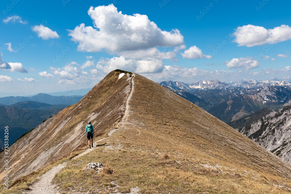 Hiker woman on idyllic hiking trail on alpine meadow with scenic view of majestic Hochschwab mountain range, Styria, Austria. Wanderlust in remote Austrian Alps. Sense of escapism, peace, reflection