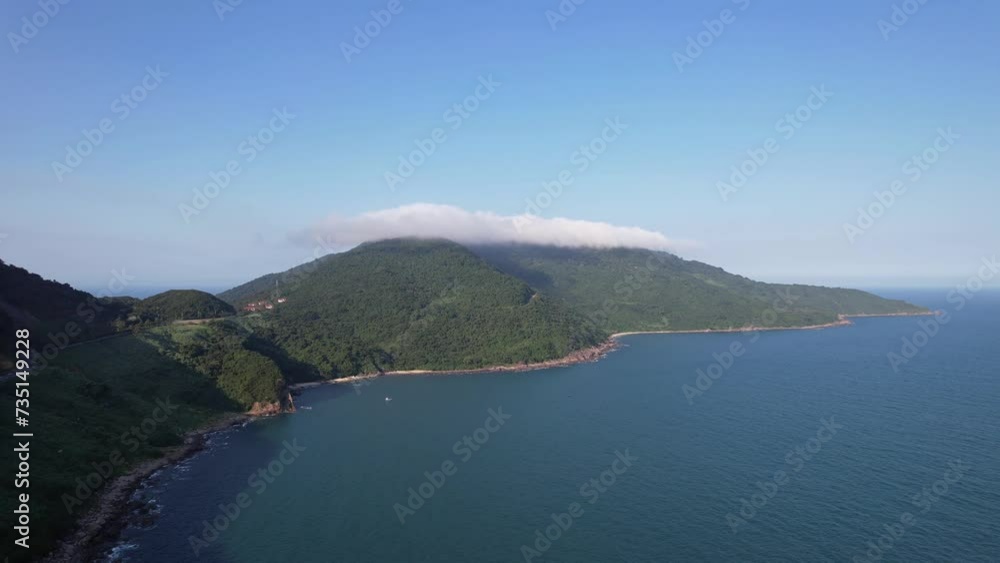 Aerial view of a serene, cloud-kissed mountainous peninsula near Da Nang, Vietnam, showcasing lush greenery and calm blue waters, recorded on February 10th, 2024 Aerial view of a serene, cloud-kissed mountainous peninsula near Da Nang, Vietnam, showcasing lush greenery and calm blue waters, recorded on February 10th, 2024