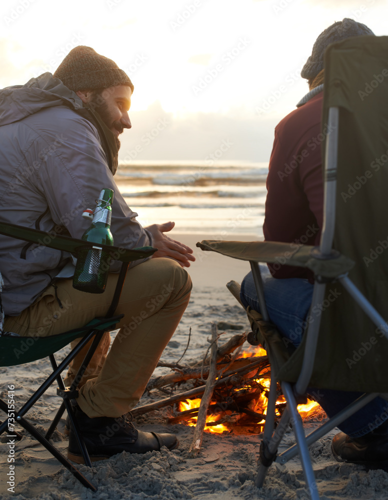 Beach, beer and fire with man friends talking on coast or shore from back for travel, holiday or vacation. Nature, camping and sunset with happy young people together on sand by sea or ocean