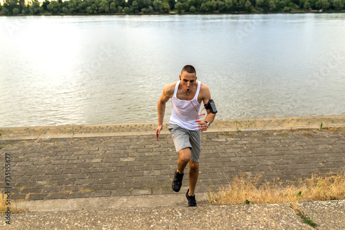 Fototapeta Naklejka Na Ścianę i Meble -  Young handsome athlete running upstairs by the river bank