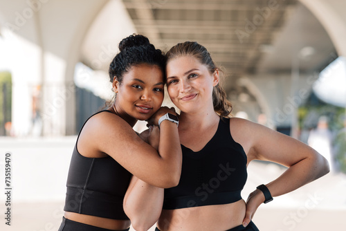 Portrait of two plus-size females in sportswear standing outdoors. Two young smiling women with similar body types hugging each other after a workout.