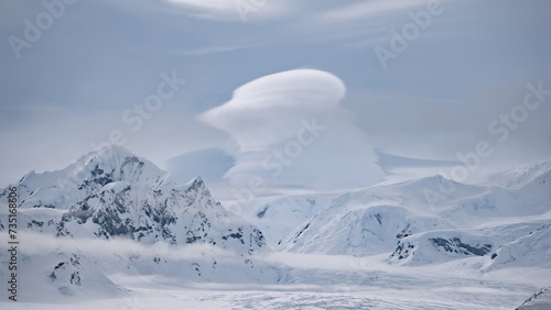 Clouds float above snow mountain ranges. Amazing Antarctic winter nature with snow capped mounts at cloudy day. Climate change and global warming concept at environment scenery of Antarctica