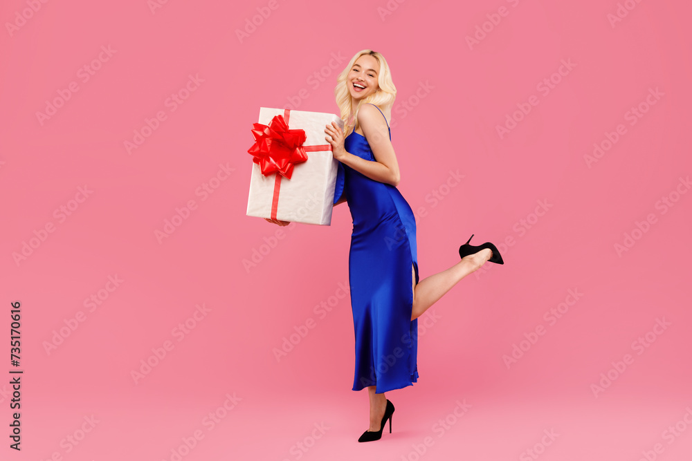 Ecstatic young woman in blue with large gift, posing on pink backdrop Ecstatic young woman in blue with large gift, posing on pink backdrop