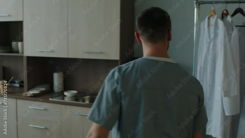 Doctor walking into break room, greeting friend with hand clasp, putting on white coat and talking to female colleague while going to work at hospital Doctor walking into break room, greeting friend with hand clasp, putting on white coat and talking to female colleague while going to work at hospital