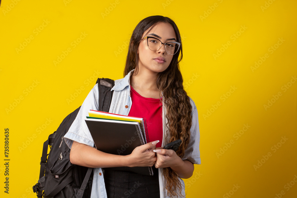 Woman, wearing glasses, denim shirt holding books and notebook with a backpack on her back Woman, wearing glasses, denim shirt holding books and notebook with a backpack on her back
