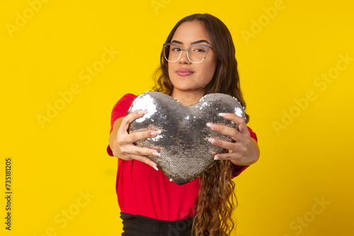 woman with long curly hair, wearing glasses and holding a heart with shiny stones