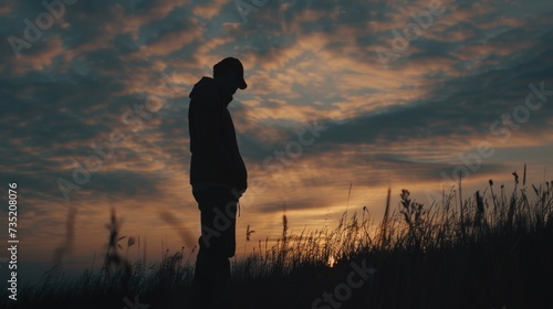 Silhouette of a person standing in a field at sunset. Perfect for nature or inspirational themes