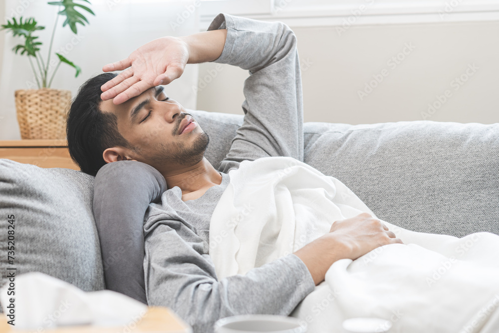 Sick, influenza asian young man, male have fever hand touching forehead for check measure body temperature, illness while lying rest on sofa at home. Health care on virus person.