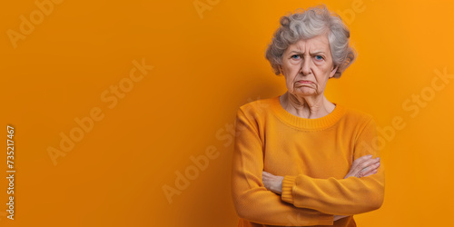 Grumpy senior woman looking at camera with resentment and disapproval, on solid background with copy space. photo