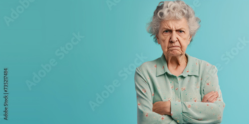 Grumpy senior woman looking at camera with resentment and disapproval, on solid background with copy space. photo