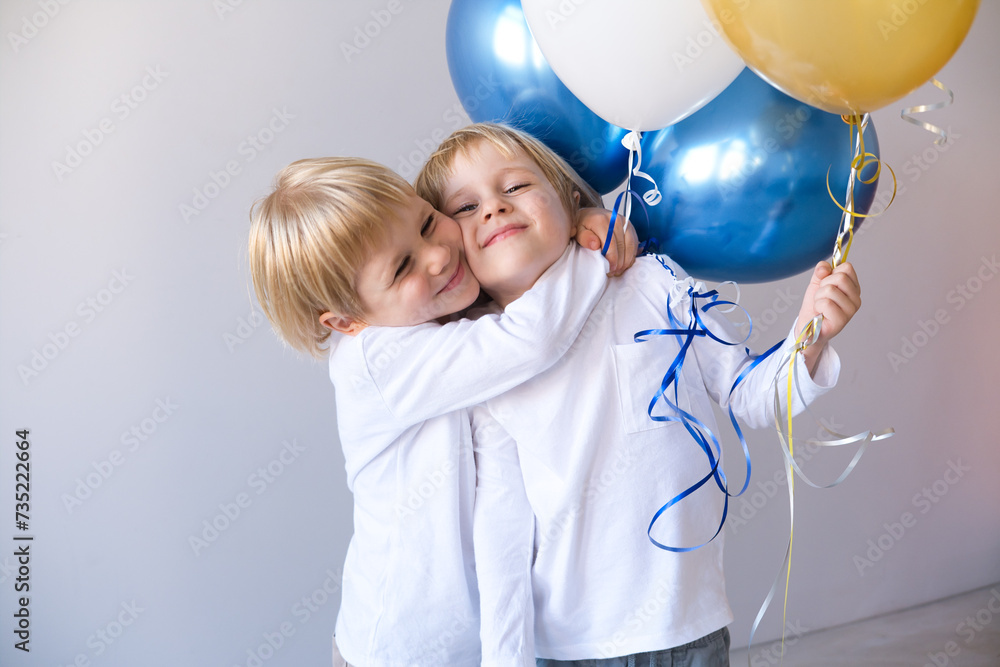 two little blonde smiling boys twins hugging, holding balloons celebration birthday two little blonde smiling boys twins hugging, holding balloons celebration birthday