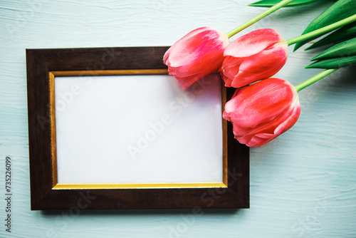 Pink tulips and mockup photo frame on wooden background. Easter or Mother's Day greeting card