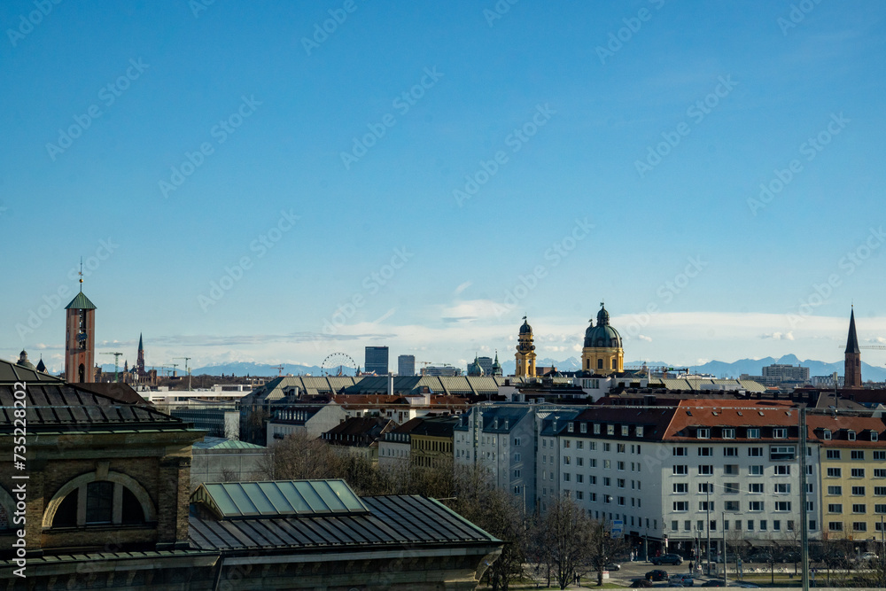 Munich skyline. View from the Technical University Munich, Germany. St. Markus on the left, the domes of the Theatiner Church on the right.  In the background the silhouette of the Alps. Blue sky