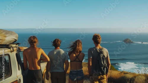 A diverse group of travelers, dressed in outdoor clothing, stand in awe at the edge of the beach, gazing out at the vast expanse of the ocean and sky, with a mountainous backdrop, as they prepare to 